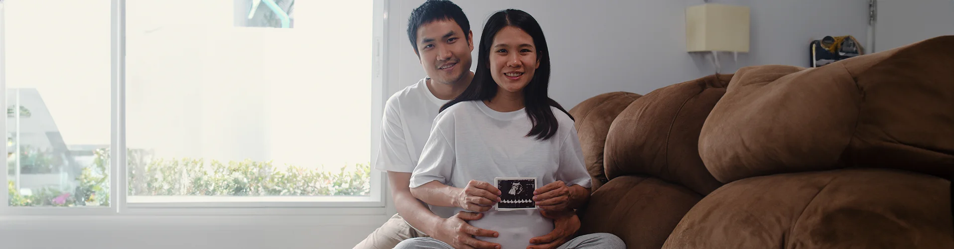 young-asian-pregnant-couple-show-looking-ultrasound-photo-baby-belly-mom-dad-feeling-happy-smiling-peaceful-while-take-care-child-lying-sofa-living-room-home-copy